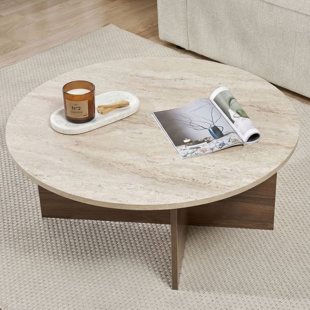 Round coffee table with travertine top and dark wooden base in cross shape.